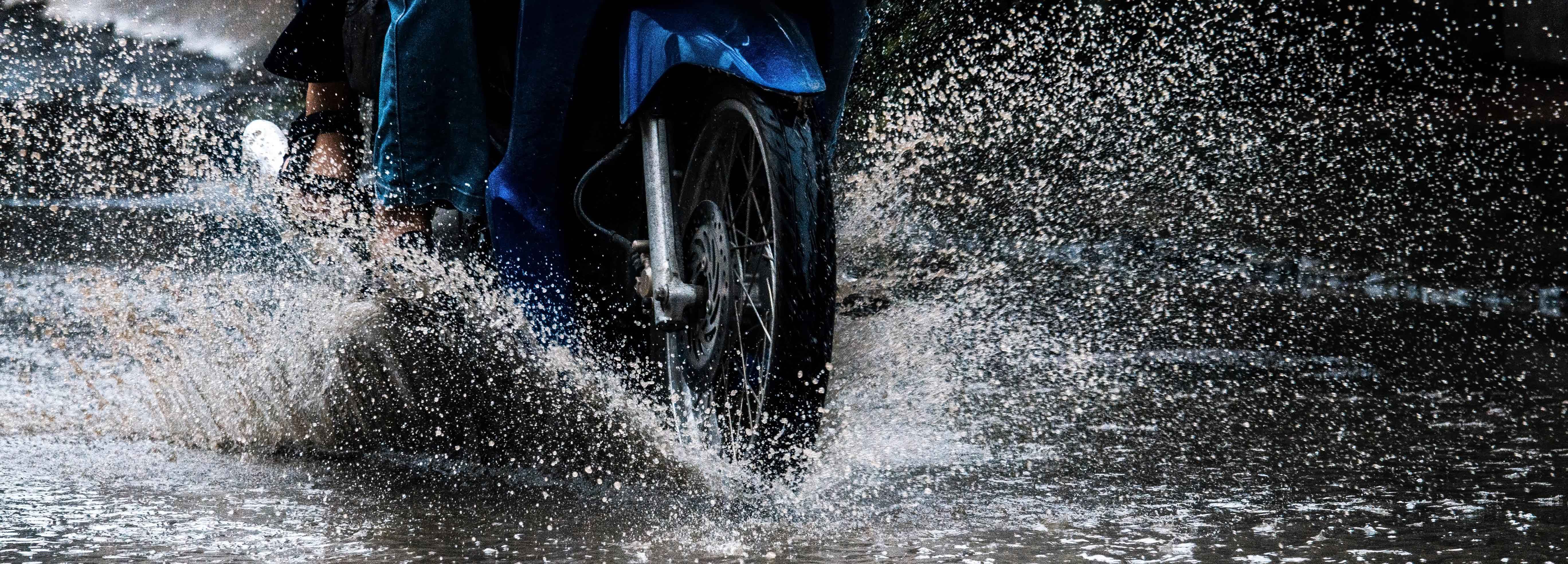 motorcycle going down the road splashing water from the front wheel in a rainstorm