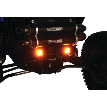 Close-up of the rear suspension and axle on an off-road RC vehicle, featuring a Moose Offroad 3" LED Light Pod Amber with two bright LEDs and visible Trinity components.