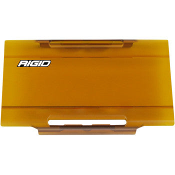 The Rigid Industries E Series Lens Cover 6 Amber is a rectangular amber plastic cover with RIGID in white on the top left, featuring a horizontal slot and a handle-like grip for easy handling.