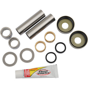 The Swingarm Bearing Kit by Pivot Works includes two metal rods, bushings, washers, seals, O-rings, and a small tube of lubricant—all meeting OEM specs and displayed on a white background.