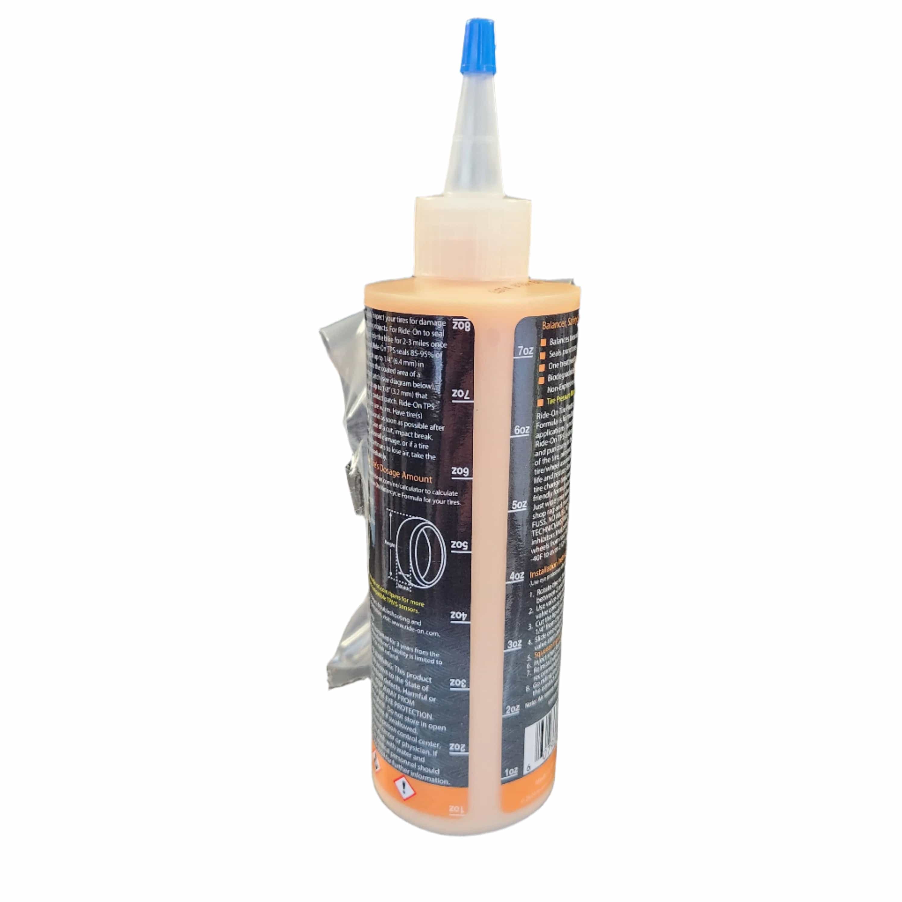 The Tire Balancer and Sealant 8oz by Ride On is a plastic bottle with a blue-tipped nozzle, partially filled with orange liquid. It features measurement markings, label text, a silver packet attached to its side, and has a plain white background.