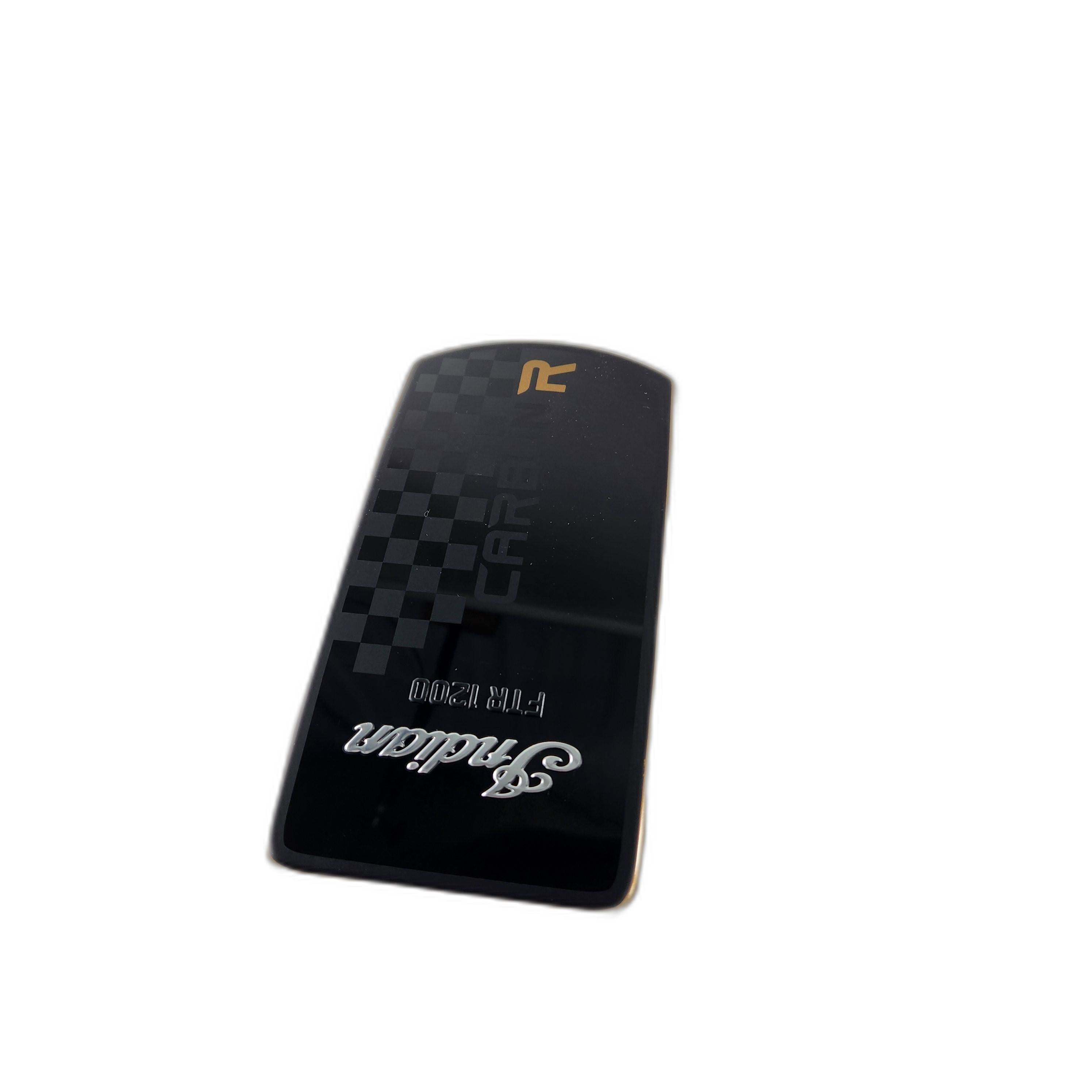 A rectangular black Cover-Bezel,Carbon,Gold [Ftr Carbon] by Polaris featuring a checkered pattern, gold and silver text, and a stylized R logo is shown against a white background; its commonly seen among OEM Indian motorcycle parts.