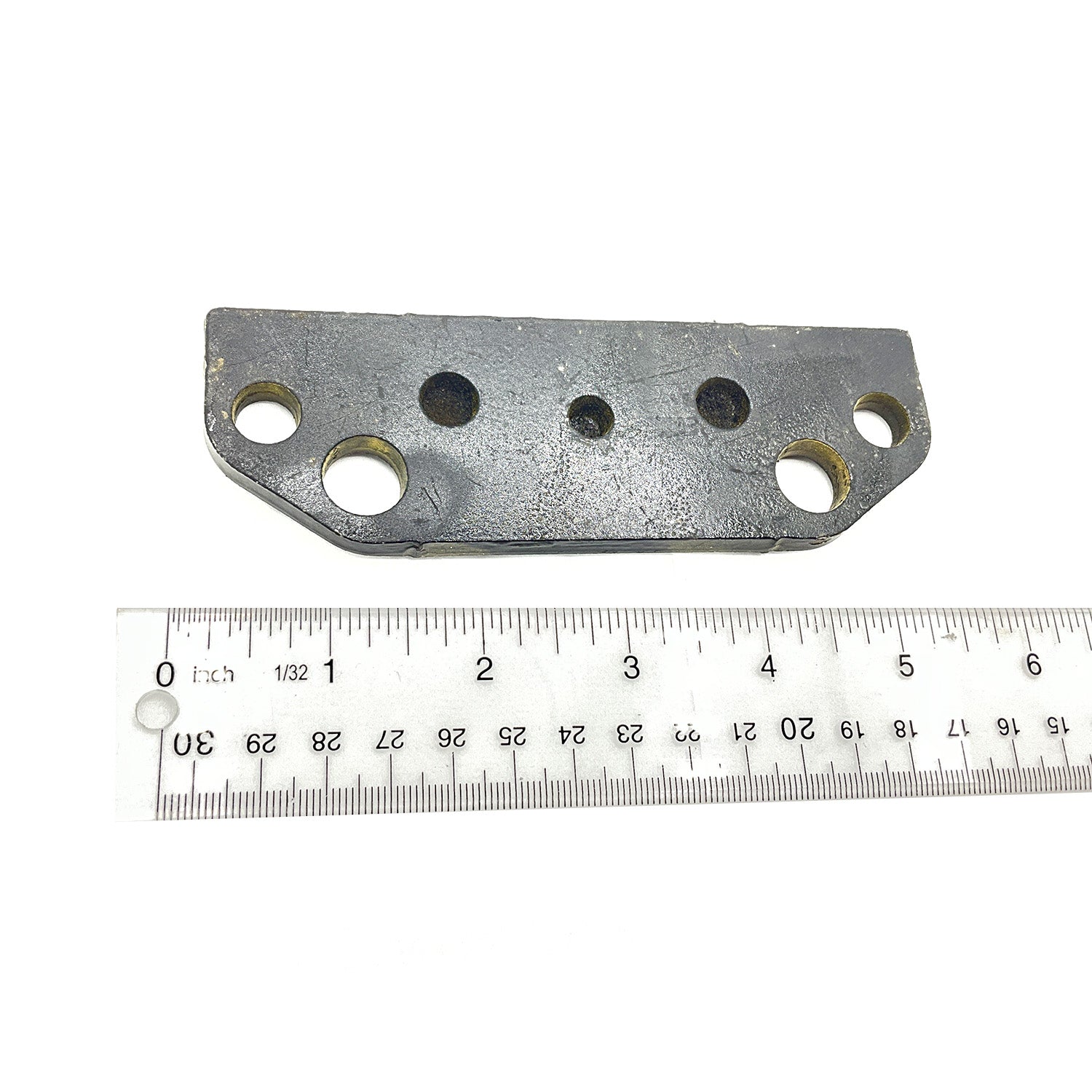 Gray metal brake pad bracket with five circular holes, positioned above a white ruler for scale.