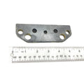 Gray metal brake pad bracket with five circular holes, positioned above a white ruler for scale.