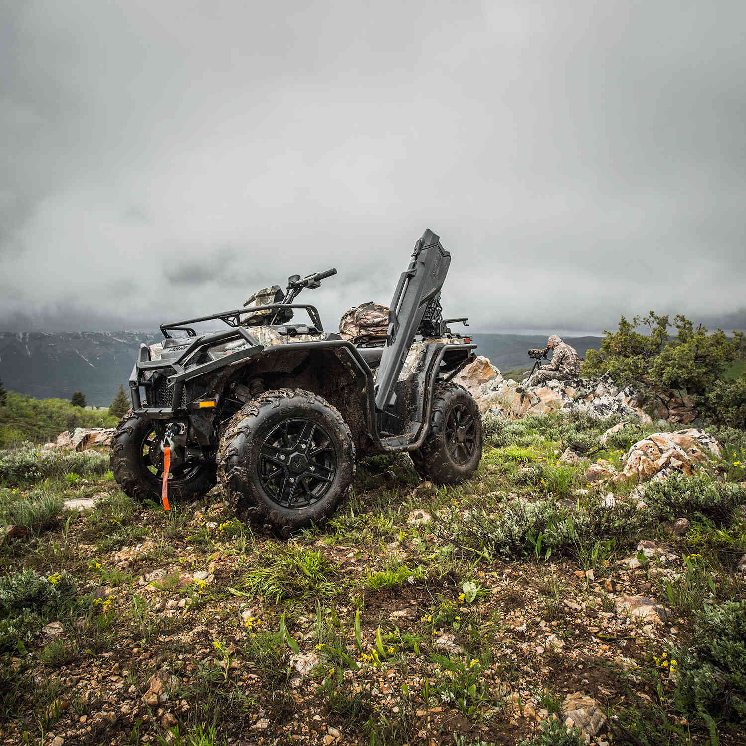 Black Polaris Sportsman XP 1000 ATV with rugged tires and mounted chainsaw on rocky terrain.