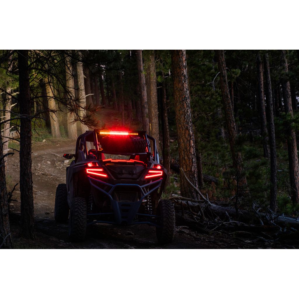 Red LED chase light bar mounted on a black Polaris off-road UTV in a forest setting at dusk.