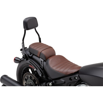 A close-up side view of a motorcycle’s rear seat with brown leather upholstery, a Detachable Backrest - Black by Cobra installed, and the rear wheel and exhaust pipe visible.
