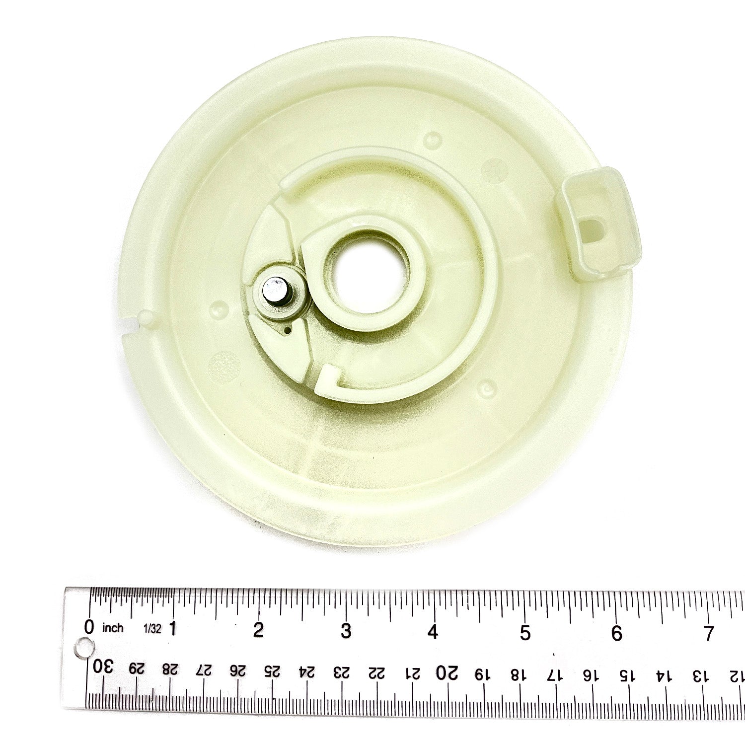 Off-white circular plastic reel with central hole and small attached metal component, shown with inch ruler for scale.