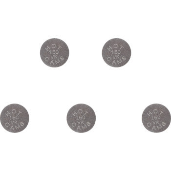 Five small, round, gray metal valve shims with stamped markings arranged in a cluster.