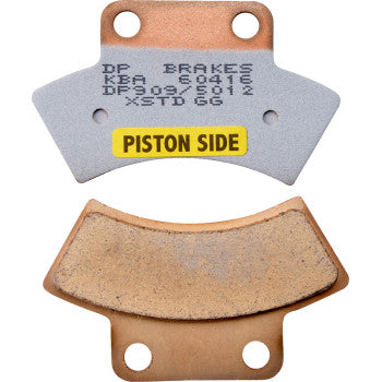 Two Sintered Brake Pads by DP Brakes are shown: one labeled PISTON SIDE with printed text and codes. Both pads have a metallic, slightly worn look and visible mounting holes at the top and bottom.