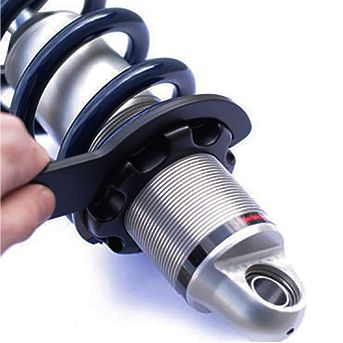 A person uses the Spanner Wrench 2.5 Backup by Fox to adjust the preload ring on a metallic coilover suspension shock absorber.
