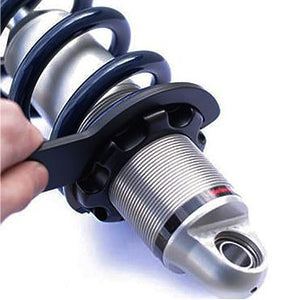 A person uses the Spanner Wrench 2.5 Backup by Fox to adjust the preload ring on a metallic coilover suspension shock absorber.