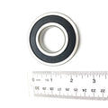 Sealed steel ball bearing with black rubber seal and silver outer ring next to a ruler for scale.