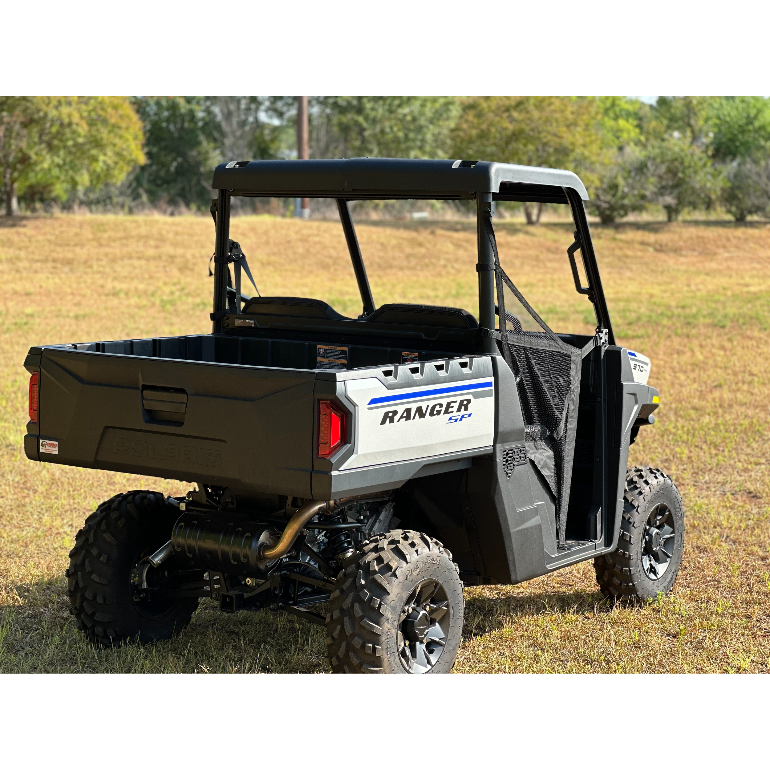 A Polaris Composit Roof by Seizmik is shown installed on a black and gray Polaris Ranger 570, parked on dry grass in an open field with trees and a clear sky visible in the background.