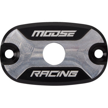 The Polaris Master Cylinder Cap by Moose Offroad is an oval 6061 aluminum part with a central hole and two side holes. It features "MOOSE" and "RACING" in white on black, offering a stylish, OEM-quality replacement.