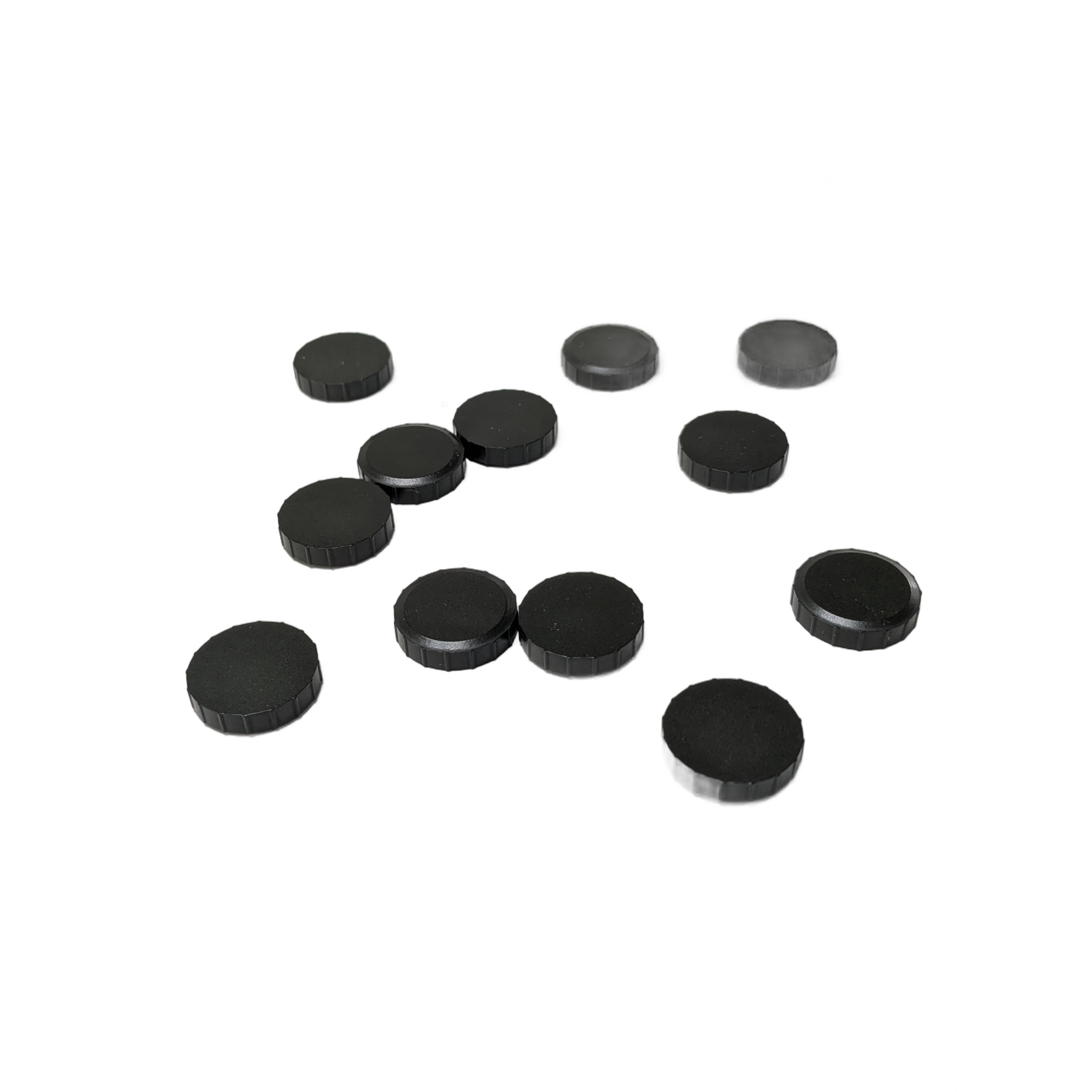 Set of small, round, black rubber caps with flat and textured surfaces scattered on white background.