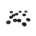 Set of small, round, black rubber caps with flat and textured surfaces scattered on white background.