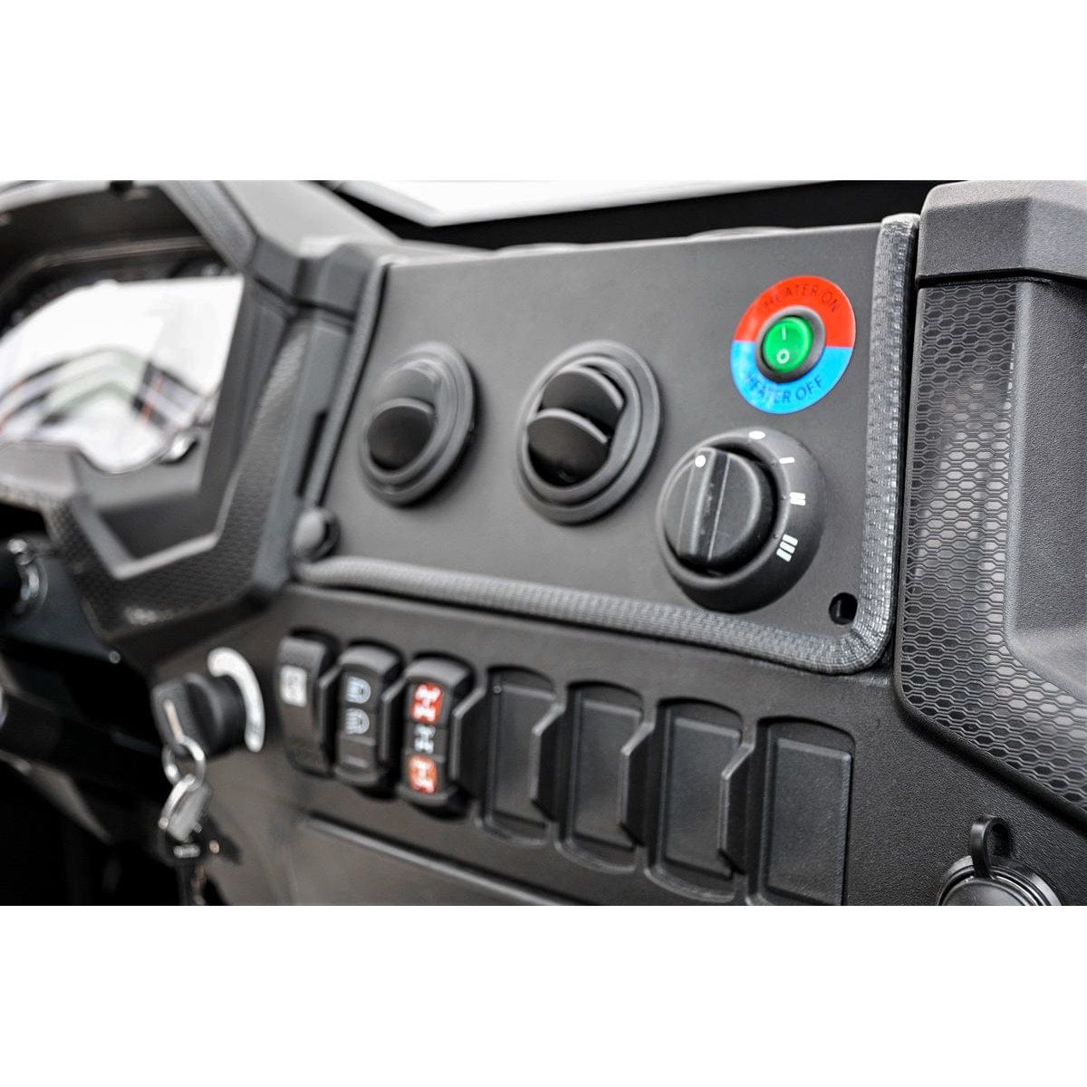 Close-up of a vehicle dashboard featuring control knobs, switches, and a large blue and red START/STOP button. The rugged UTV Cab Heater by Open Trail is shown, with polycarbonate door panels for added safety and visibility.
