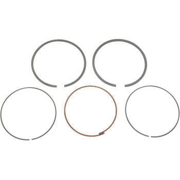 Five piston rings from the Honda Ring Set by Prox are displayed in a circular pattern on a white background, with one ring visibly textured and colored differently than the four smooth metallic OEM replacements made in Japan.