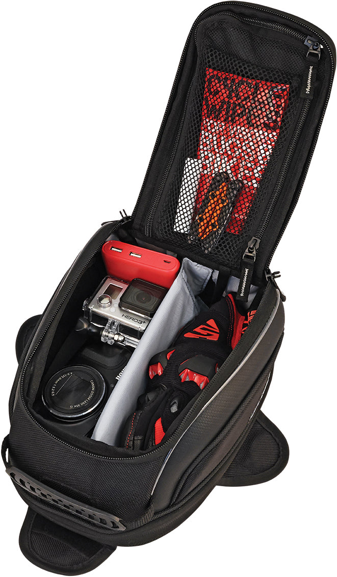 The open black Commuter Lite Tank Bag by Nelson Rigg, made of UltraMax fabric, shows organized compartments with a camera, lens, red-and-black gloves, red power bank, cords, and a small item in the mesh pocket on the lid.