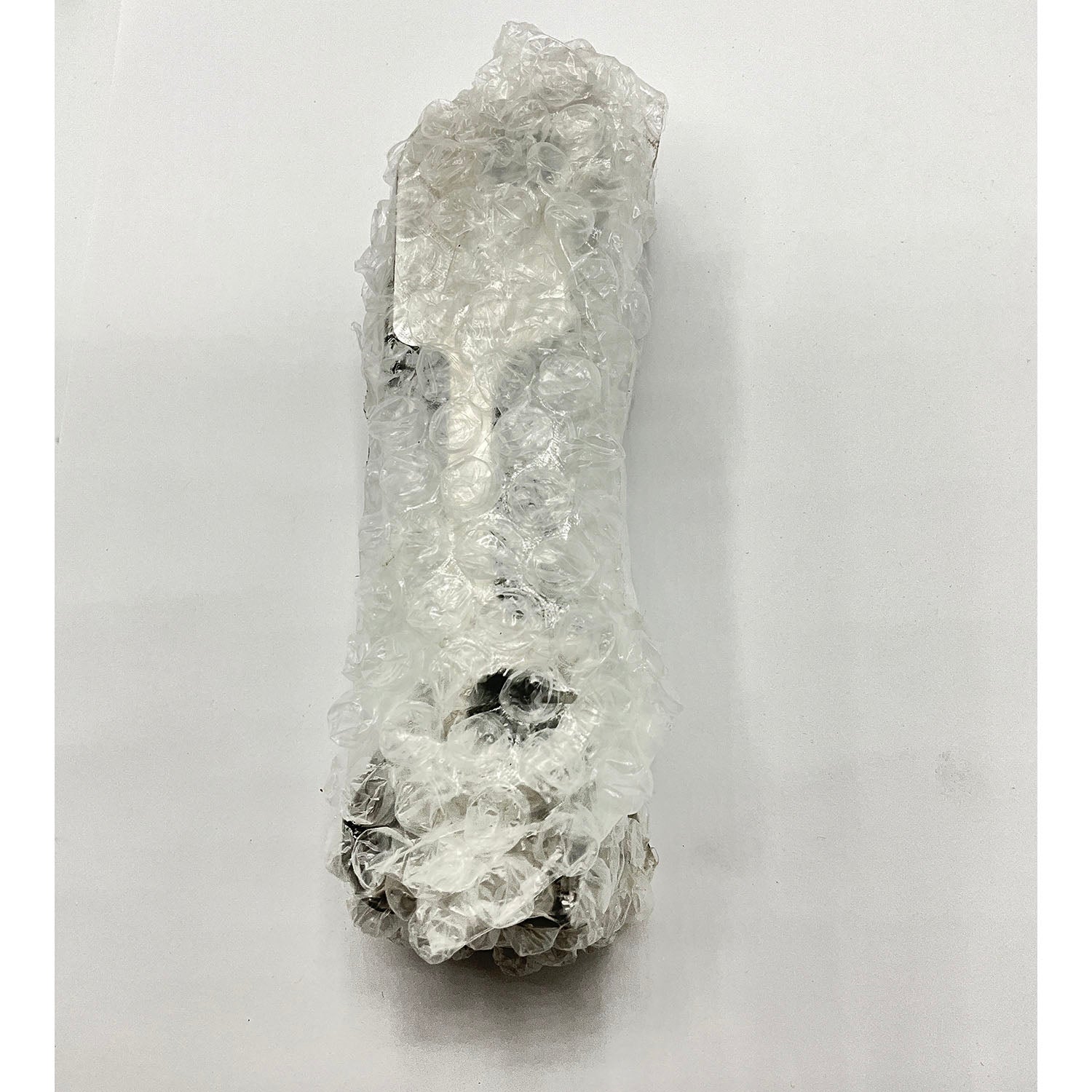 Clear plastic bubble wrap covering a long, irregular-shaped mechanical part with visible dark metal ends.