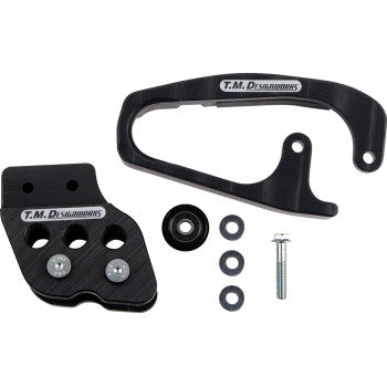 Honda TRX Chain Guide Slider Black by T.M. Designworks shown on a white background, featuring proprietary plastic, two main brackets, a small wheel, three washers, a bolt, and a nut, all T.M. Designworks branded.