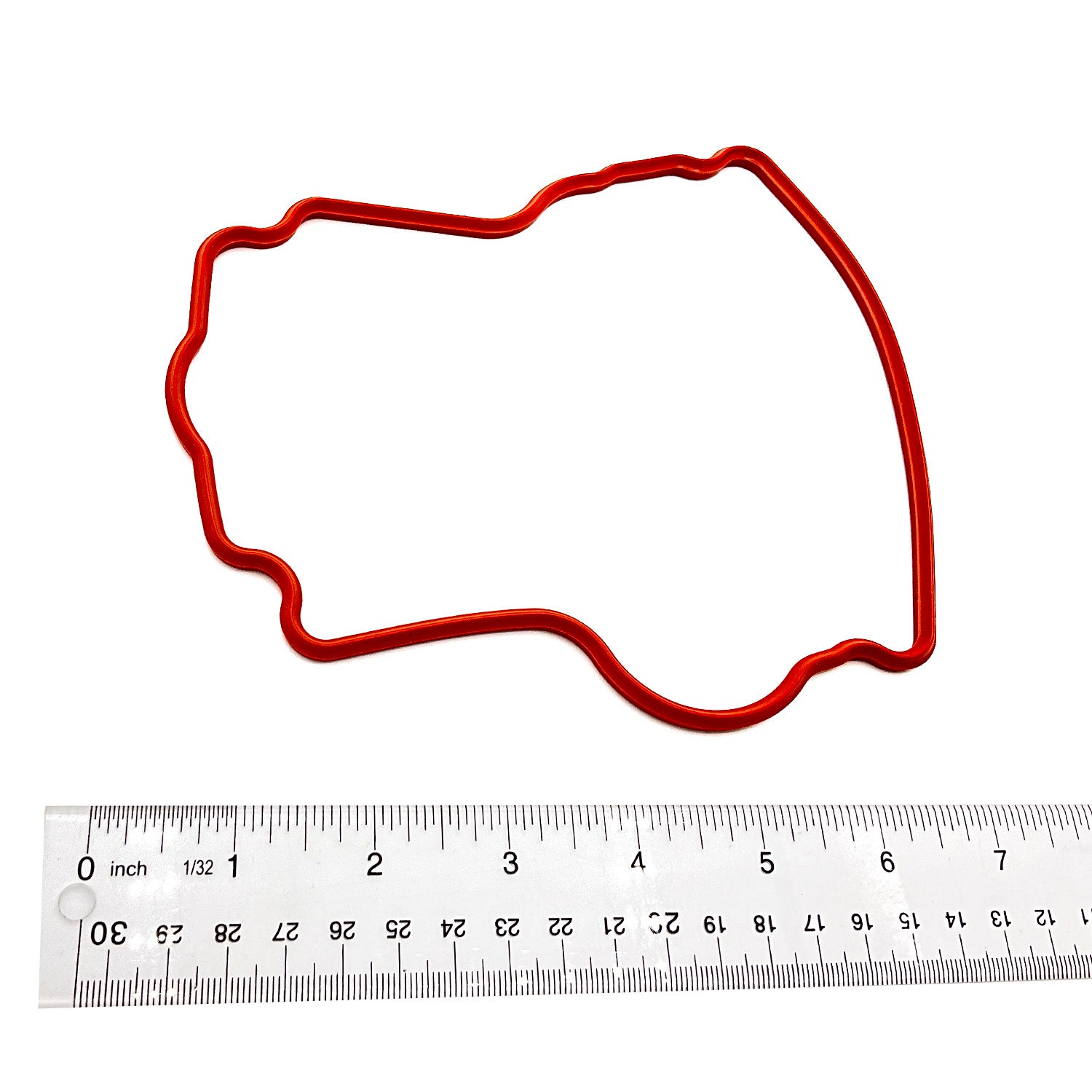 Red irregular-shaped rubber valve cover seal gasket next to a metric ruler for scale.