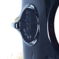 Close-up of a shiny "Headlight Bezel Paint Black Pearl by Polaris" for Indian motorcycles, featuring “Indian” engraved in cursive on a raised oval. Its lustrous surface reflects light, highlighting authentic OEM Indian Polaris parts quality.