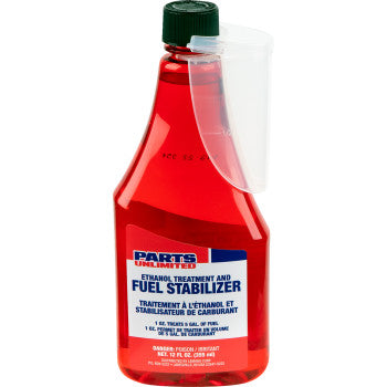 A 12 US fl oz. red bottle of Parts Unlimited Fuel Treatment and Stabilizer with a green cap and clear measuring cup; bilingual label highlights use as a fuel stabilizer for carburetor cleaning.