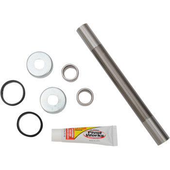 The Swingarm Bearing Kit by Pivot Works includes a metal rod, two washers, two seals, two bushings, two black O-rings, and a tube of grease, all arranged on a white background.