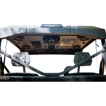 View from the rear of an off-road vehicle with two empty seats and a Can Am Defender Audio Shade by Hoppe Industries, featuring 4 speakers, 1 subwoofer, Bluetooth marine receiver, LED light bar, and roof-mounted control panels.