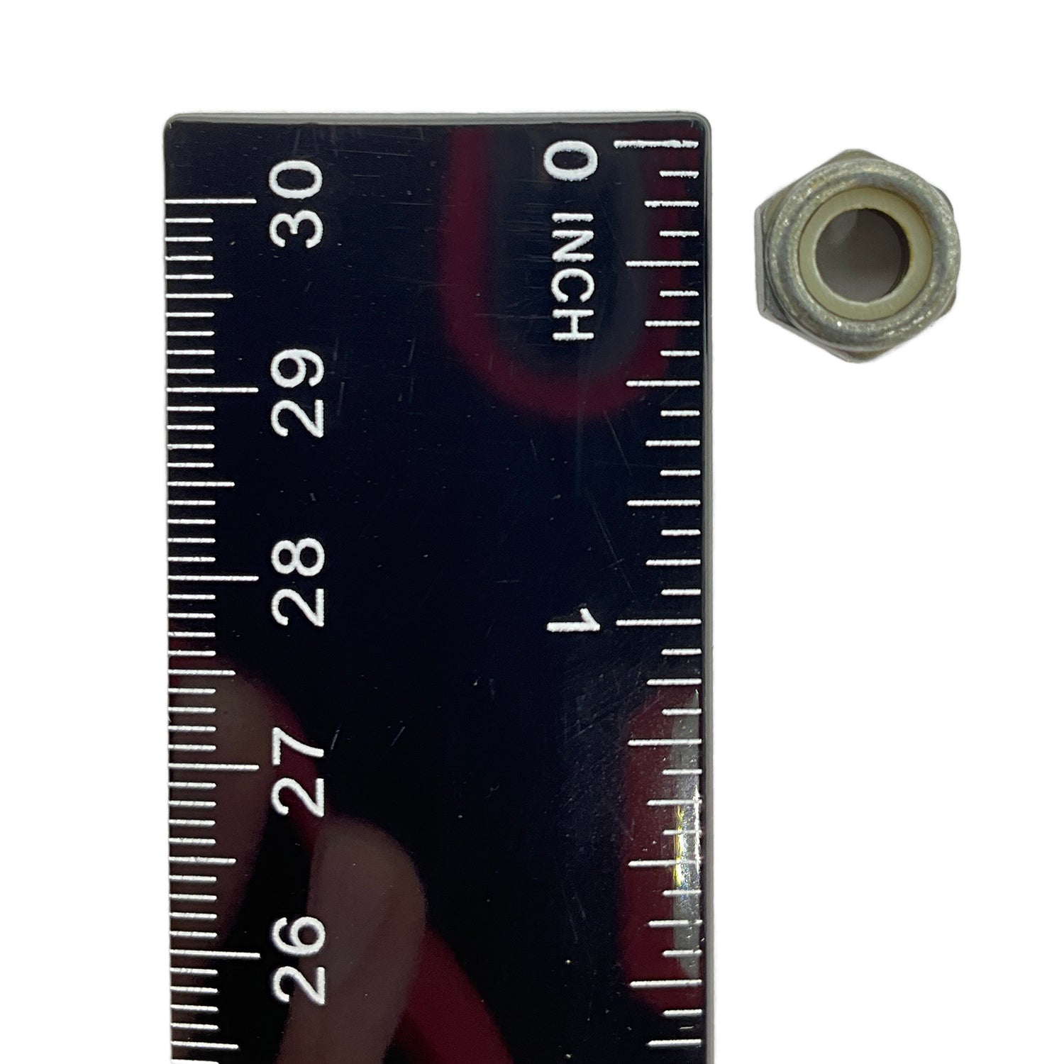Small hexagonal metal nut with nylon insert, placed next to a black ruler showing size under 1 inch.