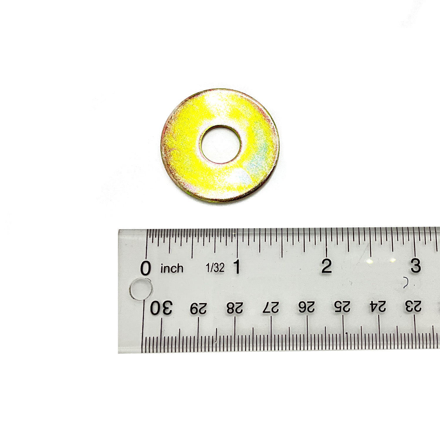 Yellow-gold metal flat washer with central hole beside clear plastic ruler marked in inches and centimeters.