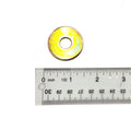 Yellow-gold metal flat washer with central hole beside clear plastic ruler marked in inches and centimeters.