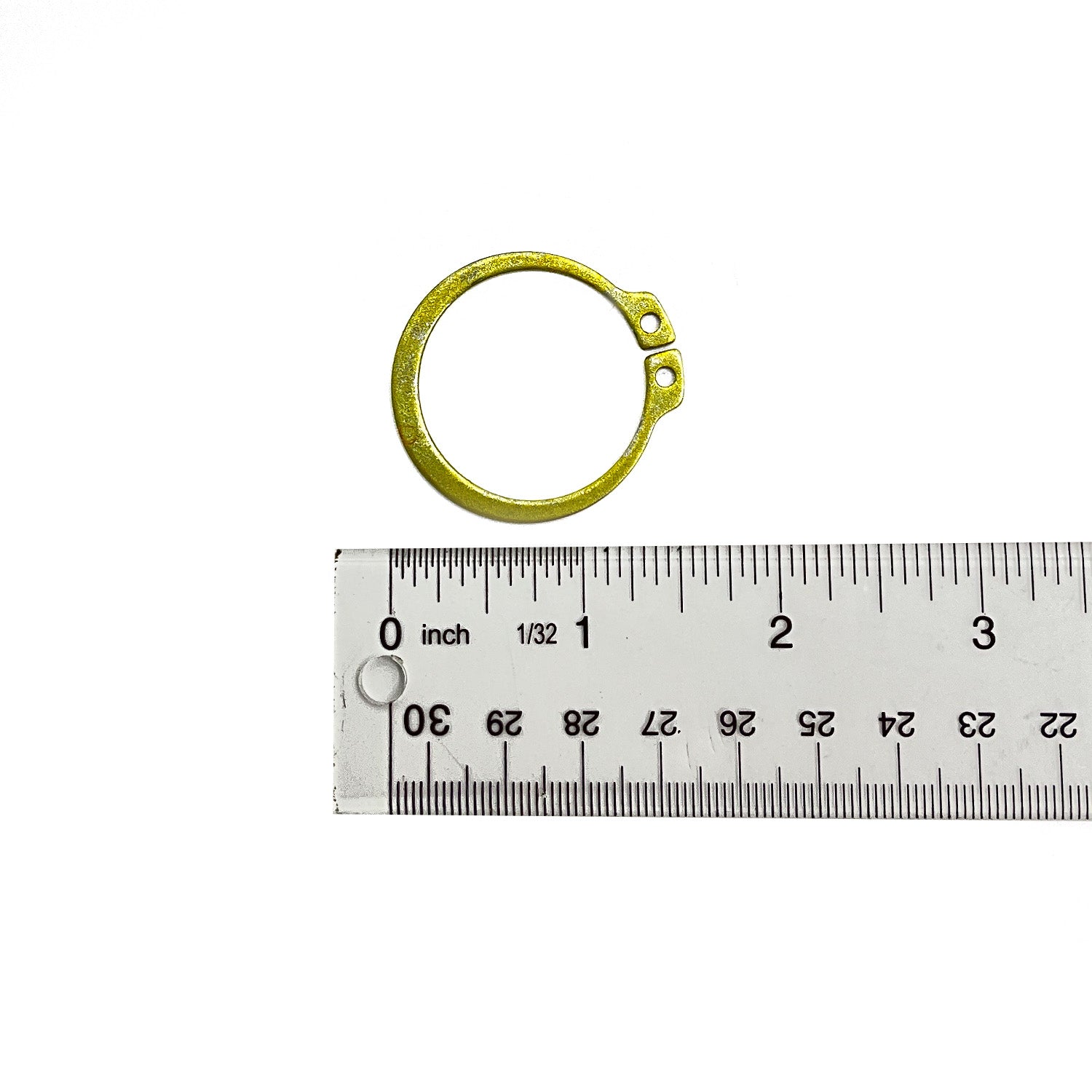 Small circular brass retaining ring with two holes, placed next to a clear ruler showing measurements in inches and.