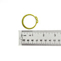 Small circular brass retaining ring with two holes, placed next to a clear ruler showing measurements in inches and.