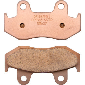Two copper-colored Yamaha Standard Brake Pads by DP Brakes are shown: one displays the engraved model number DP966 XSTD 511627, while the other highlights its textured friction surface.