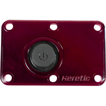 A rectangular, metallic red switch plate with a black power button at the center, designed for the Lens Dome Light Red by Heretic. Features four corner holes and "Heretic" engraved in the lower right corner.