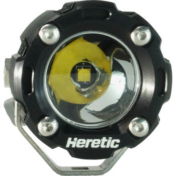Close-up of the Light Pod Spot by Heretic, a round black LED light with a center yellow Cree LED, silver screws around the rim, and "Heretic" on the bottom edge of its aircraft-grade aluminum frame.