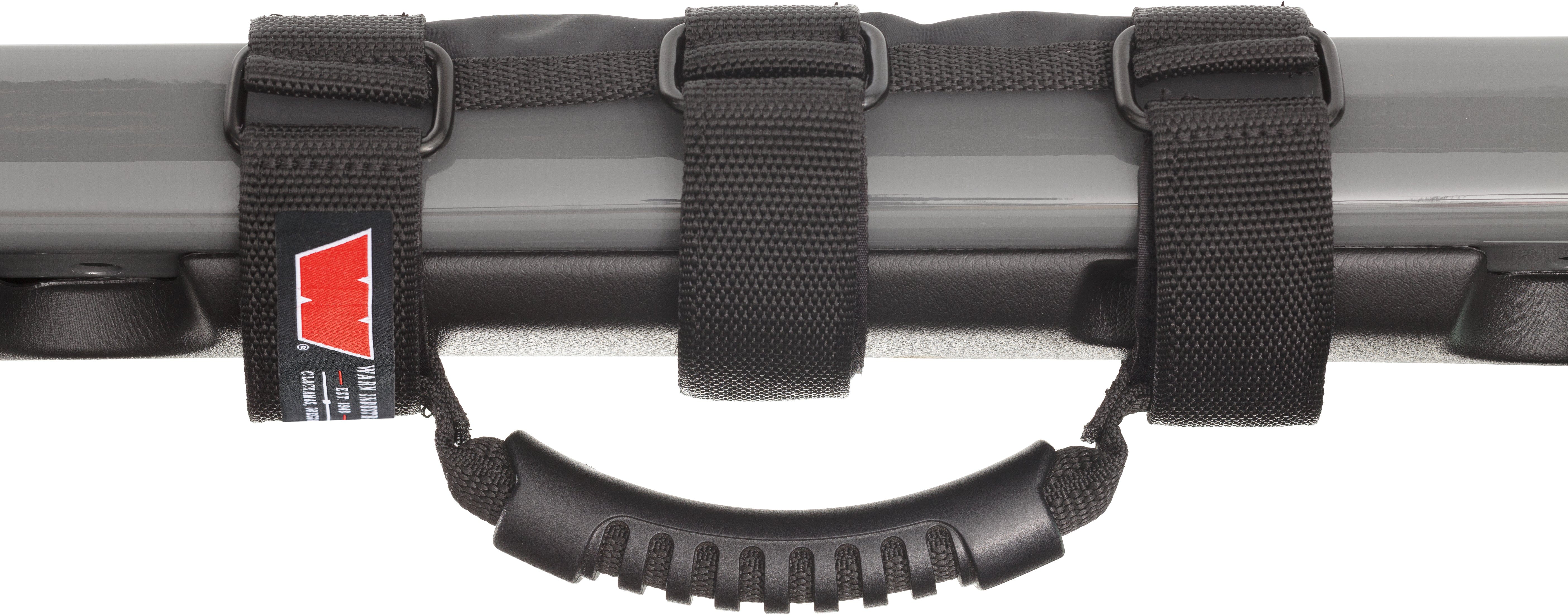 The Warn Roll Bar Grab Handles feature a black nylon handle with a rubber grip, adjustable black straps with plastic buckles on a gray metal bar, marine-grade construction, and a visible red and white tag on one strap.