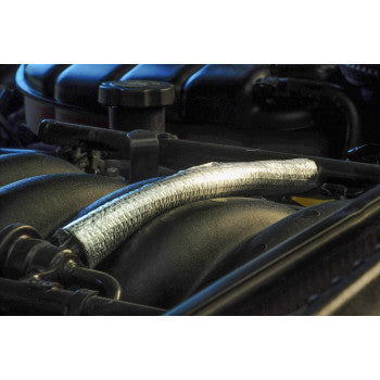 A close-up view of a car engine featuring the Vapor Block Sleeve - 1/2 x 36 by DEI installed on a hose, providing insulation, heat protection, and preventing vapor lock.