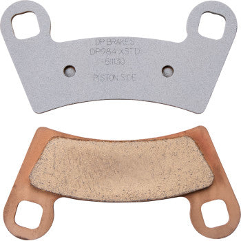 Two metallic Polaris Standard Brake Pads by Dp Brakes are shown: one with a flat silver surface and stamped text, the other with a copper-colored backing and textured friction surface, highlighting their durable sintered metal design.