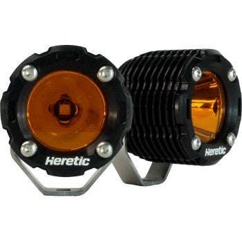 The Light Pods Amber Spot Pair by Heretic features two round black LED lights with orange lenses, aircraft-grade aluminum brackets, and "Heretic" printed on the front. Shown from both front and side angles.