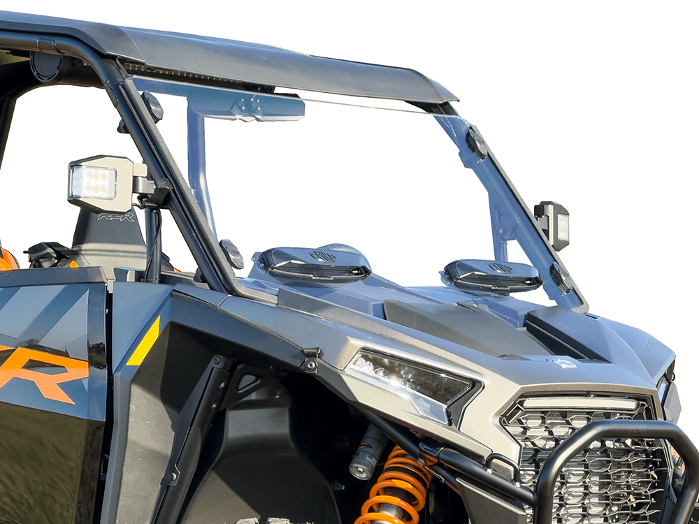 A close-up of a Polaris RZR XP/XP-4 1000 featuring a Spike dual vented hard coated front windshield, LED lights, orange suspension springs, and black and gray panels with yellow and orange accents for the ultimate off-road adventure.