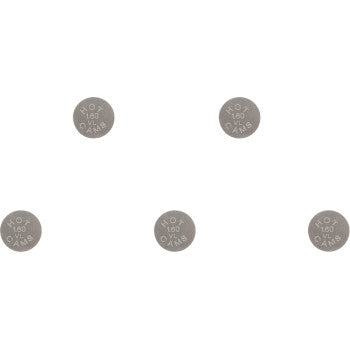 Five small, round, silver metal valve shims with engraved size markings, arranged in a scattered pattern.