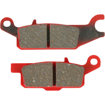 Red metal backing plates with gray carbon brake pad friction surfaces, rectangular with rounded edges and mounting holes.