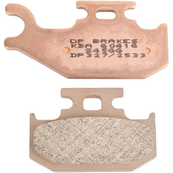 Two Standard Brake Pads Yamaha Kodiak by DP Brakes are shown—one displays stamped text, the other reveals its textured friction surface. These ATV brake pads have unique shapes with notches and cutouts for fitting.