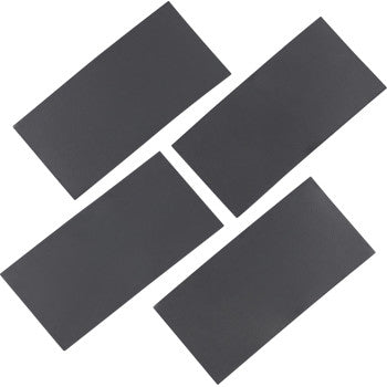 Four rectangular black brake pad shims with smooth surfaces and uniform thickness arranged in a staggered layout.