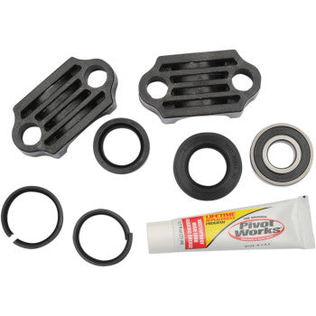 The Steering Stem Bearing Kit by Pivot Works features two black metal plates, seals, a precision machined bearing, retaining rings, and a tube of grease, all arranged on a white background.