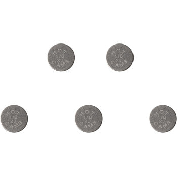 Five small, round, metallic valve shims with engraved size markings, arranged on white background.